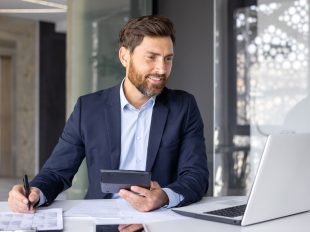 uomo in giacca prende appunti a mano consultando smartphone e laptop