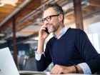 uomo sorridente parla al telefono e consulta il suo laptop