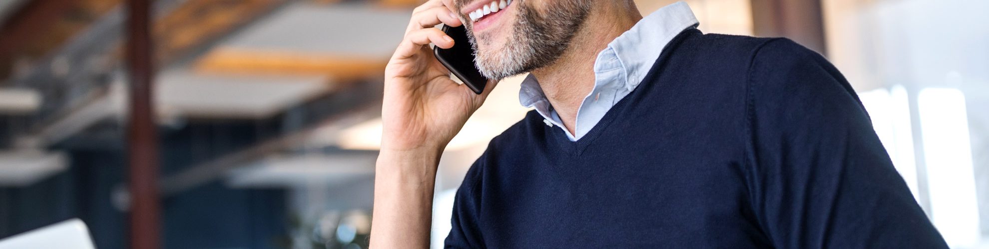 uomo sorridente parla al telefono e consulta il suo laptop